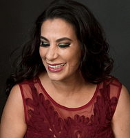 A photographic portrait of Maysoon Zayid. She has shoulder length brown hair, is smiling and wearing a maroon garment.